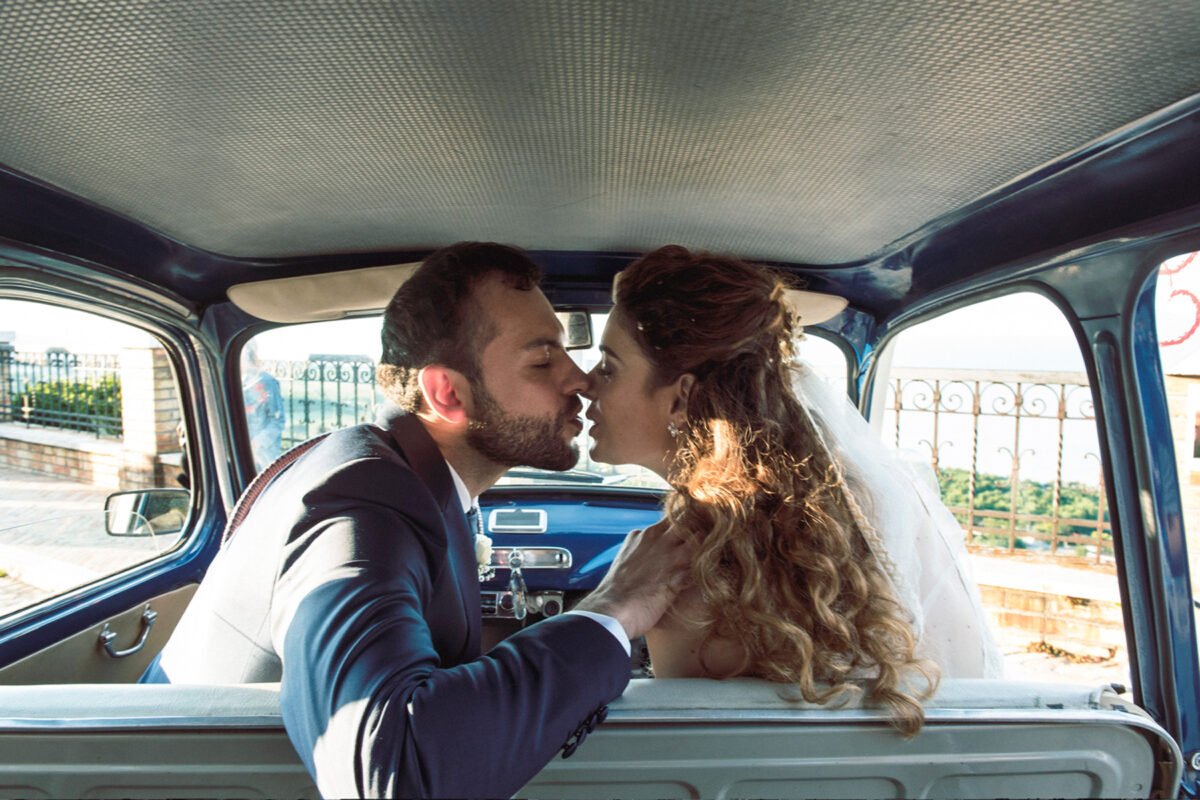 Bride and groom kissing in a vintage car during their wedding in Torre di Palme