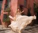Darya Osho in a handmade wedding dress by Atelier Zolotas, flowing in the air in an epic way against a traditional house in the Plaka district, Athens